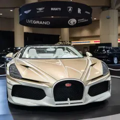 Ein goldener Bugatti Roadster mit weißen Ledersitzen steht auf einer Messe. Die Frage "wie schnell ist ein Bugatti?" wird hier durch die Präsenz dieses Supersportwagens aufgeworfen.