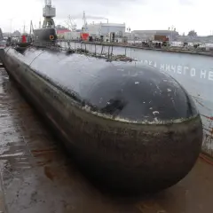 Ein riesiges U-Boot, das schnellste U-Boot der Welt, liegt im Trockendock. Im Hintergrund sind Kräne und andere Schiffe zu sehen.