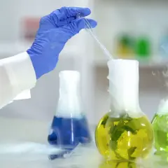 Laborant mit blauer Handschuh tropft Flüssigkeit in Kolben, wo chemische Reaktionen im Alltag Dampf erzeugen.