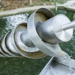 Eine Archimedes-Schraube hebt Wasser aus einem Teich. Das Wasser fließt über die spiralförmigen Windungen und wird nach oben transportiert.