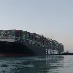 Ein riesiges Evergreen-Containerschiff, die "Ever Given", wird von einem Schlepper durch ruhiges Wasser gezogen.