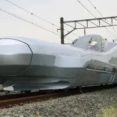 Der futuristisch anmutende, silberne Zug, der aussieht wie der schnellste Zug der Welt, steht auf Gleisen. Mehrere Personen sind auf Leitern, um ihn zu inspizieren.
