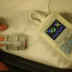 Ein Finger ist mit einem Pulsoximeter verbunden, um den Sauerstoffgehalt im Blut zu messen. Das Gerät zeigt 96% SpO2 und 68 BPM an.