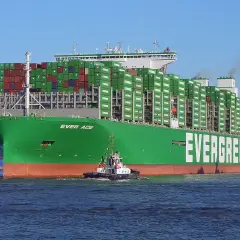 Ein riesiges grünes Containerschiff der Reederei Evergreen, die "Ever Age", wird von einem Schlepper durch das Wasser gezogen. Die technischen Daten sind beeindruckend.