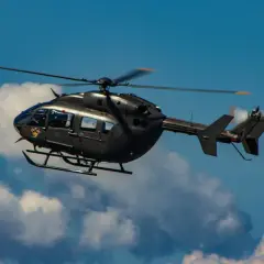 Ein dunkler Militärhubschrauber fliegt schnell durch den blauen Himmel mit Wolken.