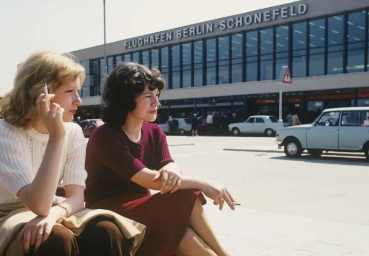 Zwei Frauen rauchen vor dem Flughafen Berlin-Schönefeld. Die Bauzeit des Flughafens war lang, aber die Aussicht ist es wert.