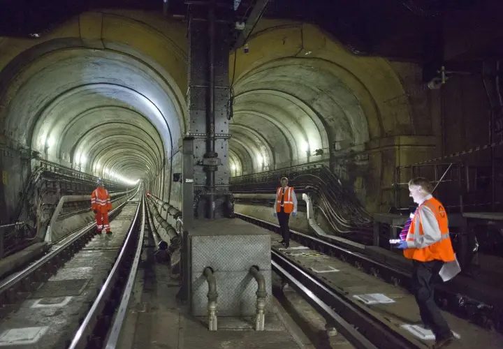 Arbeiter inspizieren den historischen Thames Tunnel. Die gewölbte Tunnelkonstruktion mit Gleisen und Beleuchtung ist beeindruckend.