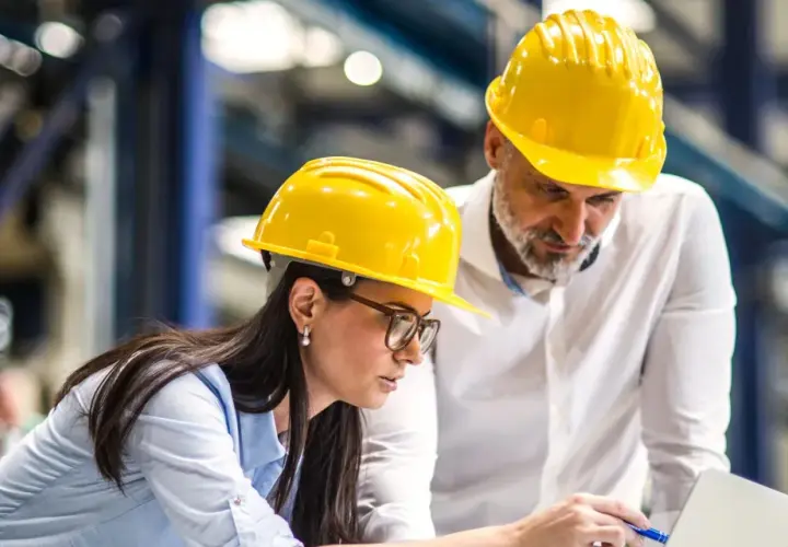 Zwei Bauingenieure mit gelben Helmen besprechen Pläne am Laptop. Sie planen, was ein Bauingenieur macht.