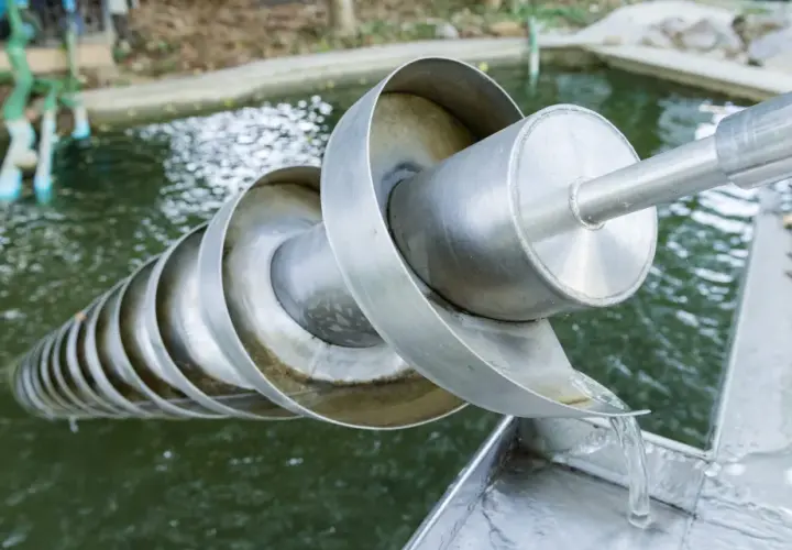 Eine Archimedes-Schraube hebt Wasser aus einem Teich. Das Wasser fließt über die spiralförmigen Windungen und wird nach oben transportiert.