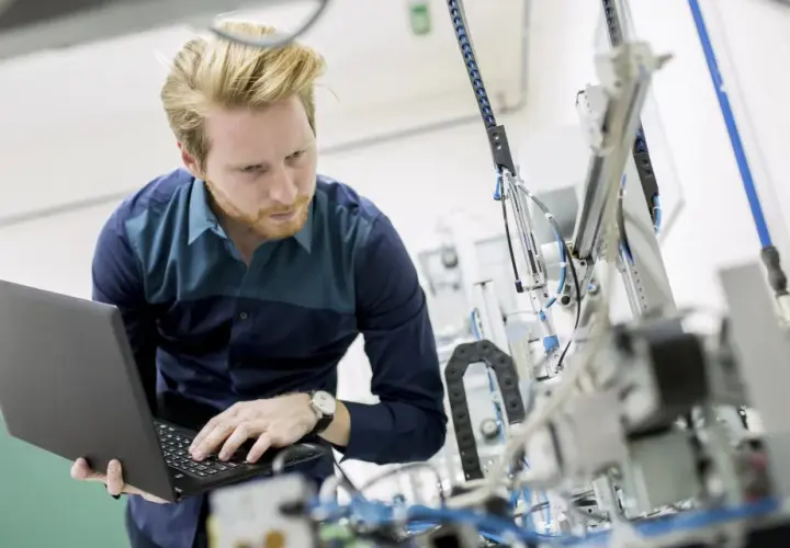 Ingenieur mit Laptop vor komplexer Maschine. So machen Ingenieure Technik greifbar und entwickeln Lösungen.