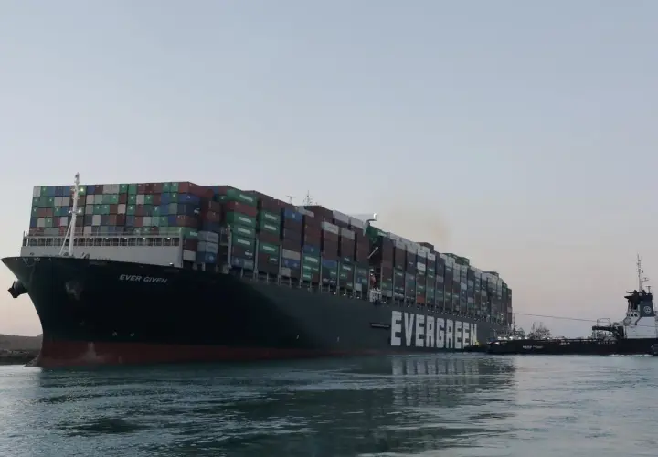 Ein riesiges Evergreen-Containerschiff, die "Ever Given", wird von einem Schlepper durch ruhiges Wasser gezogen.