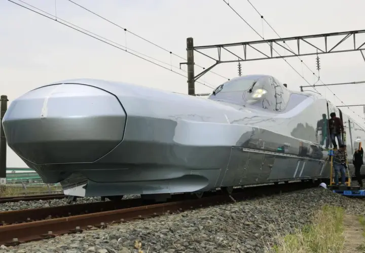 Der futuristisch anmutende, silberne Zug, der aussieht wie der schnellste Zug der Welt, steht auf Gleisen. Mehrere Personen sind auf Leitern, um ihn zu inspizieren.
