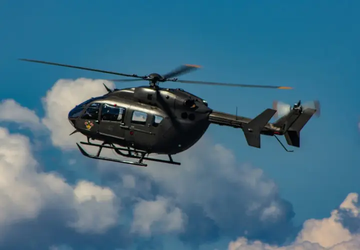 Ein dunkler Militärhubschrauber fliegt schnell durch den blauen Himmel mit Wolken.