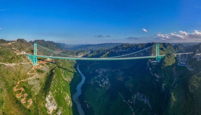 Die Huajiang Grand Canyon Bridge überspannt eine tiefe Schlucht mit einem Fluss. Die Brücke ist ein Meisterwerk der Ingenieurskunst in einer atemberaubenden Berglandschaft.