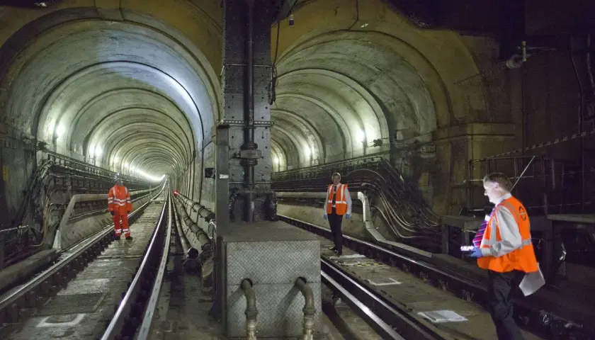 Arbeiter inspizieren den historischen Thames Tunnel. Die gewölbte Tunnelkonstruktion mit Gleisen und Beleuchtung ist beeindruckend.