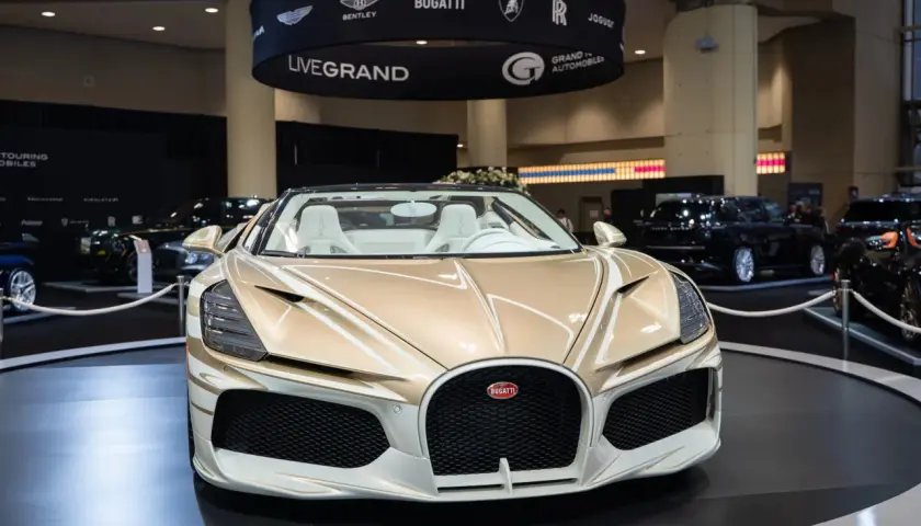 Ein goldener Bugatti Roadster mit weißen Ledersitzen steht auf einer Messe. Die Frage "wie schnell ist ein Bugatti?" wird hier durch die Präsenz dieses Supersportwagens aufgeworfen.