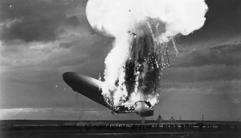 Ein Zeppelin stürzt brennend ab, eine riesige Explosion reißt ihn auseinander. Zuschauer stehen fassungslos am Boden.