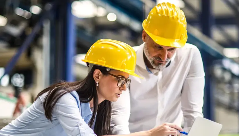 Zwei Bauingenieure mit gelben Helmen besprechen Pläne am Laptop. Sie planen, was ein Bauingenieur macht.