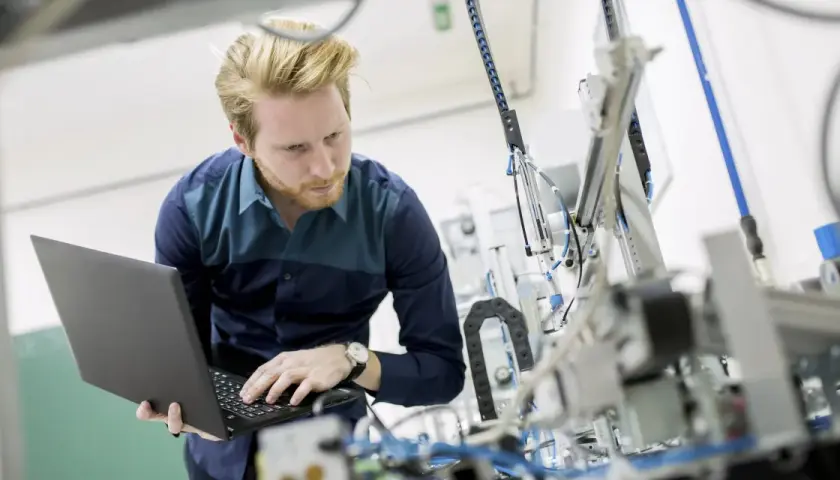 Ingenieur mit Laptop vor komplexer Maschine. So machen Ingenieure Technik greifbar und entwickeln Lösungen.