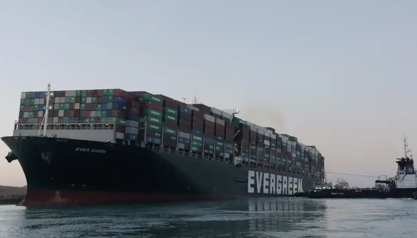Ein riesiges Evergreen-Containerschiff, die "Ever Given", wird von einem Schlepper durch ruhiges Wasser gezogen.
