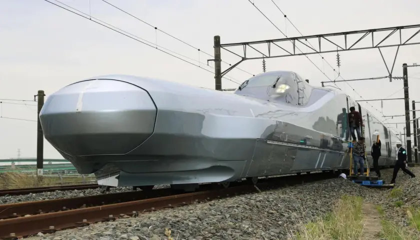 Der futuristisch anmutende, silberne Zug, der aussieht wie der schnellste Zug der Welt, steht auf Gleisen. Mehrere Personen sind auf Leitern, um ihn zu inspizieren.