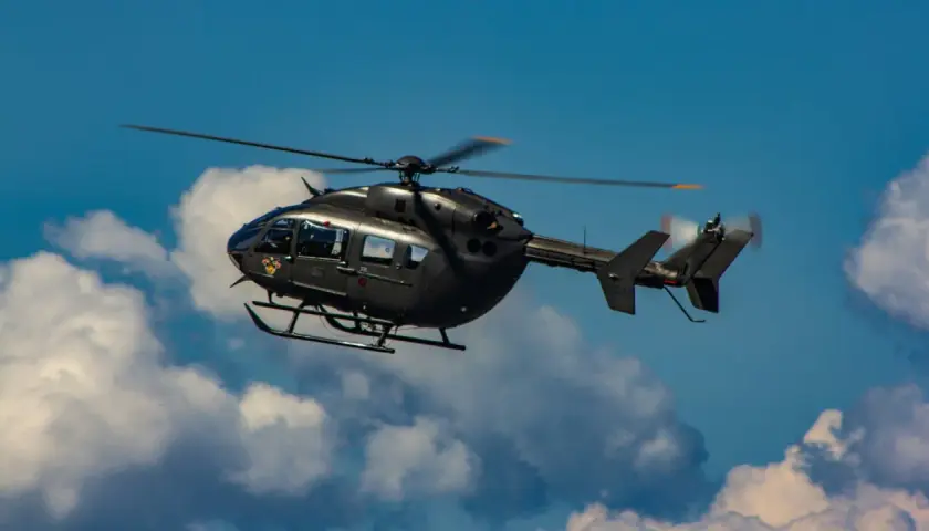Ein dunkler Militärhubschrauber fliegt schnell durch den blauen Himmel mit Wolken.