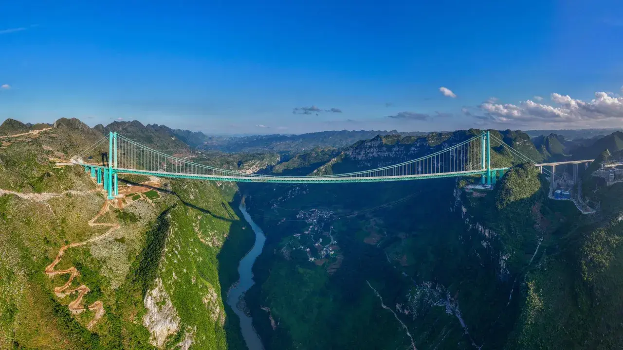 Die Huajiang Grand Canyon Bridge überspannt eine tiefe Schlucht mit einem Fluss. Die Brücke ist ein Meisterwerk der Ingenieurskunst in einer atemberaubenden Berglandschaft.