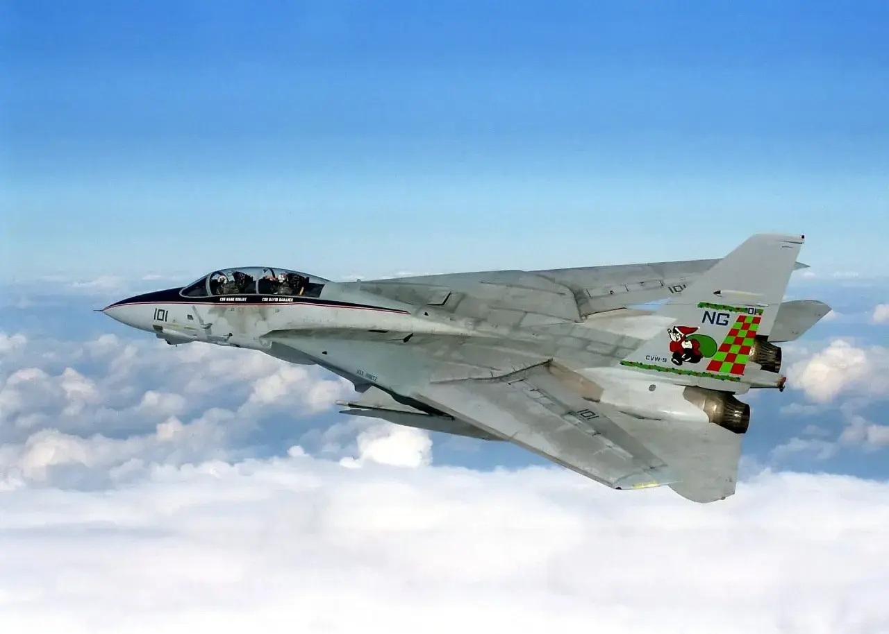 Ein schnelles Flugzeug, eine F-14 Tomcat, fliegt über den Wolken. Das Flugzeug hat eine markante Lackierung mit einer Figur auf dem Heck.