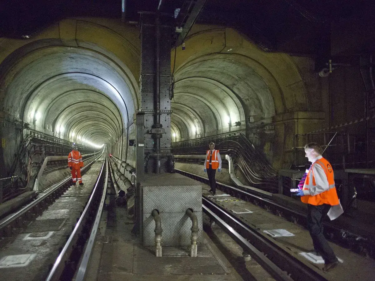 Arbeiter inspizieren den historischen Thames Tunnel. Die gewölbte Tunnelkonstruktion mit Gleisen und Beleuchtung ist beeindruckend.