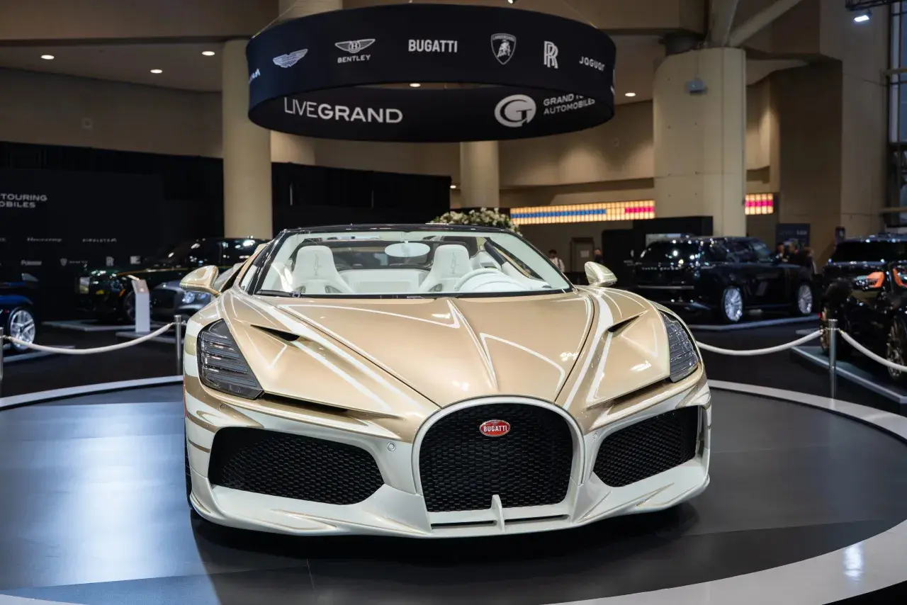 Ein goldener Bugatti Roadster mit weißen Ledersitzen steht auf einer Messe. Die Frage "wie schnell ist ein Bugatti?" wird hier durch die Präsenz dieses Supersportwagens aufgeworfen.