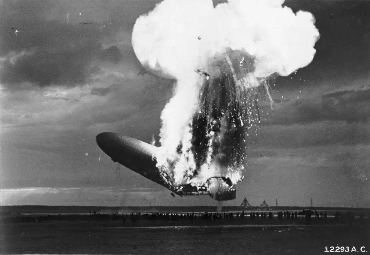 Ein Zeppelin stürzt brennend ab, eine riesige Explosion reißt ihn auseinander. Zuschauer stehen fassungslos am Boden.