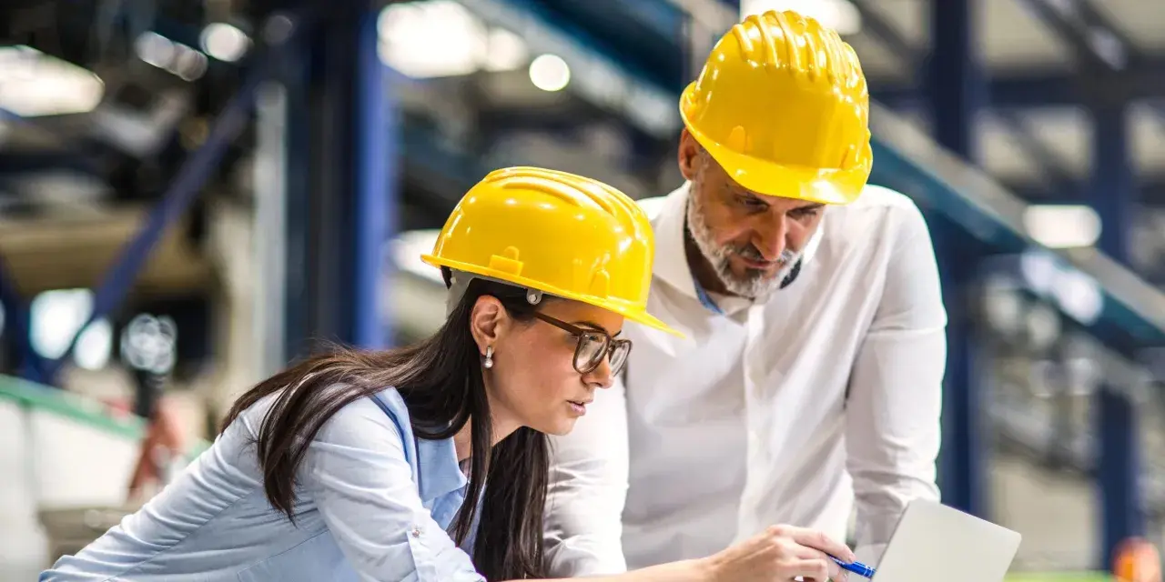 Zwei Bauingenieure mit gelben Helmen besprechen Pläne am Laptop. Sie planen, was ein Bauingenieur macht.