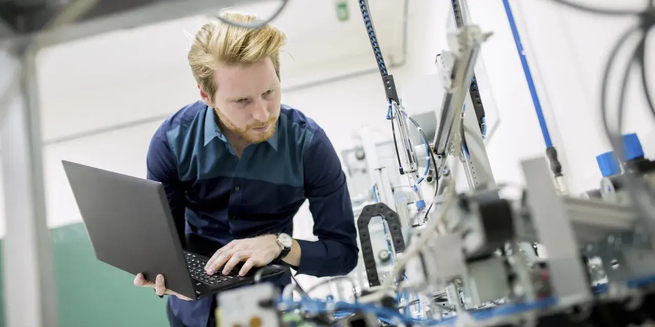 Ingenieur mit Laptop vor komplexer Maschine. So machen Ingenieure Technik greifbar und entwickeln Lösungen.