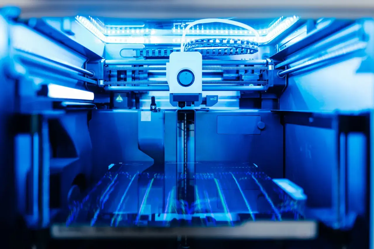 Ein 3D-Drucker im Einsatz, der durch additive Fertigung komplexe Strukturen erschafft. Das blaue Licht beleuchtet die Präzision des 3D-Drucks.