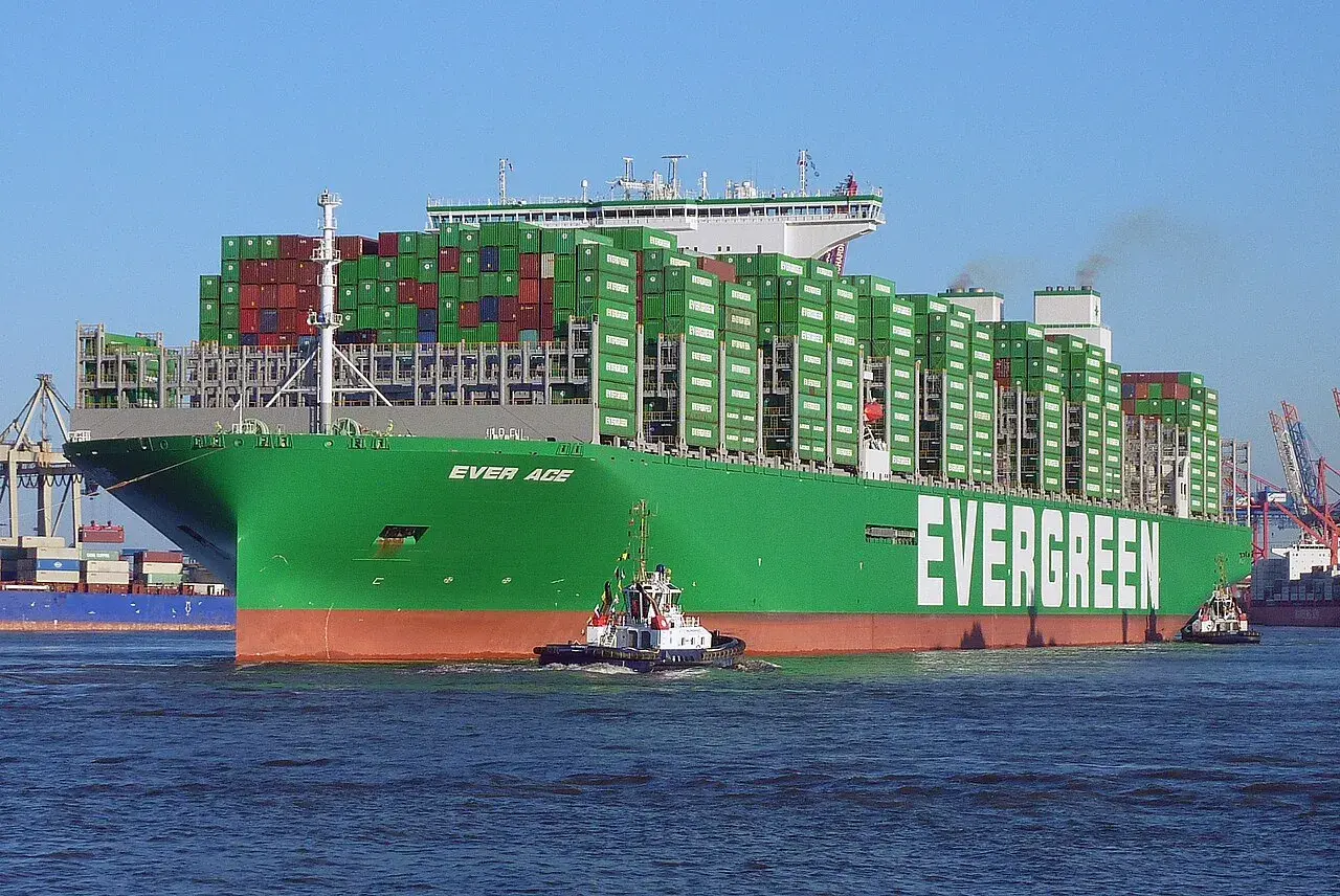Ein riesiges grünes Containerschiff der Reederei Evergreen, die "Ever Age", wird von einem Schlepper durch das Wasser gezogen. Die technischen Daten sind beeindruckend.