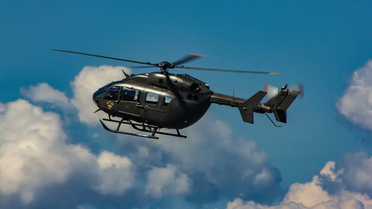 Ein dunkler Militärhubschrauber fliegt schnell durch den blauen Himmel mit Wolken.