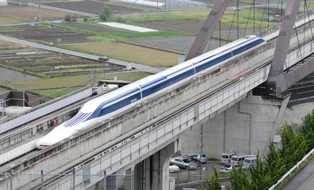 Der schnellste Zug Japans, ein Magnetschwebezug, rast &uuml;ber eine erh&ouml;hte Strecke. Felder und eine Stra&szlig;e mit Autos sind im Hintergrund zu sehen.
