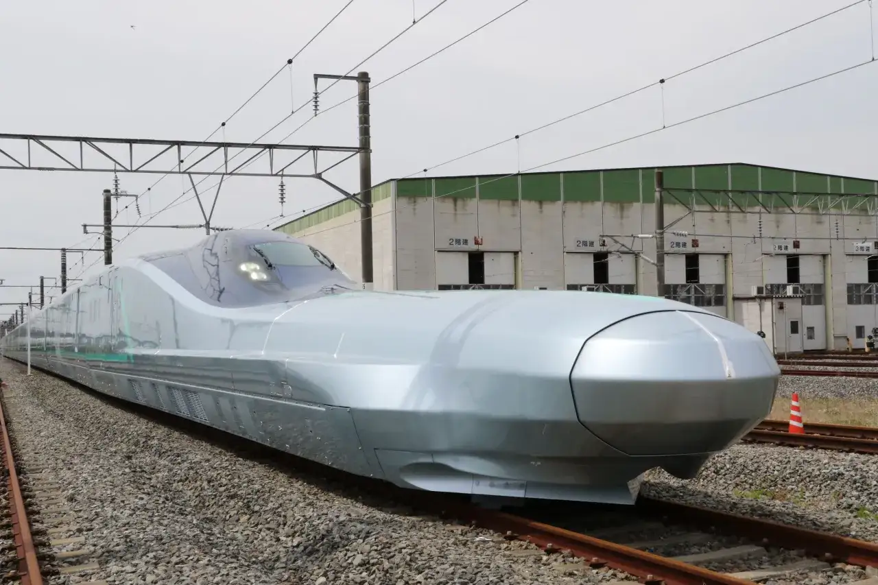 Ein futuristischer Shinkansen-Zug steht auf Gleisen vor einer Lagerhalle. Seine aerodynamische Form verspricht unglaubliche shinkansen geschwindigkeit.