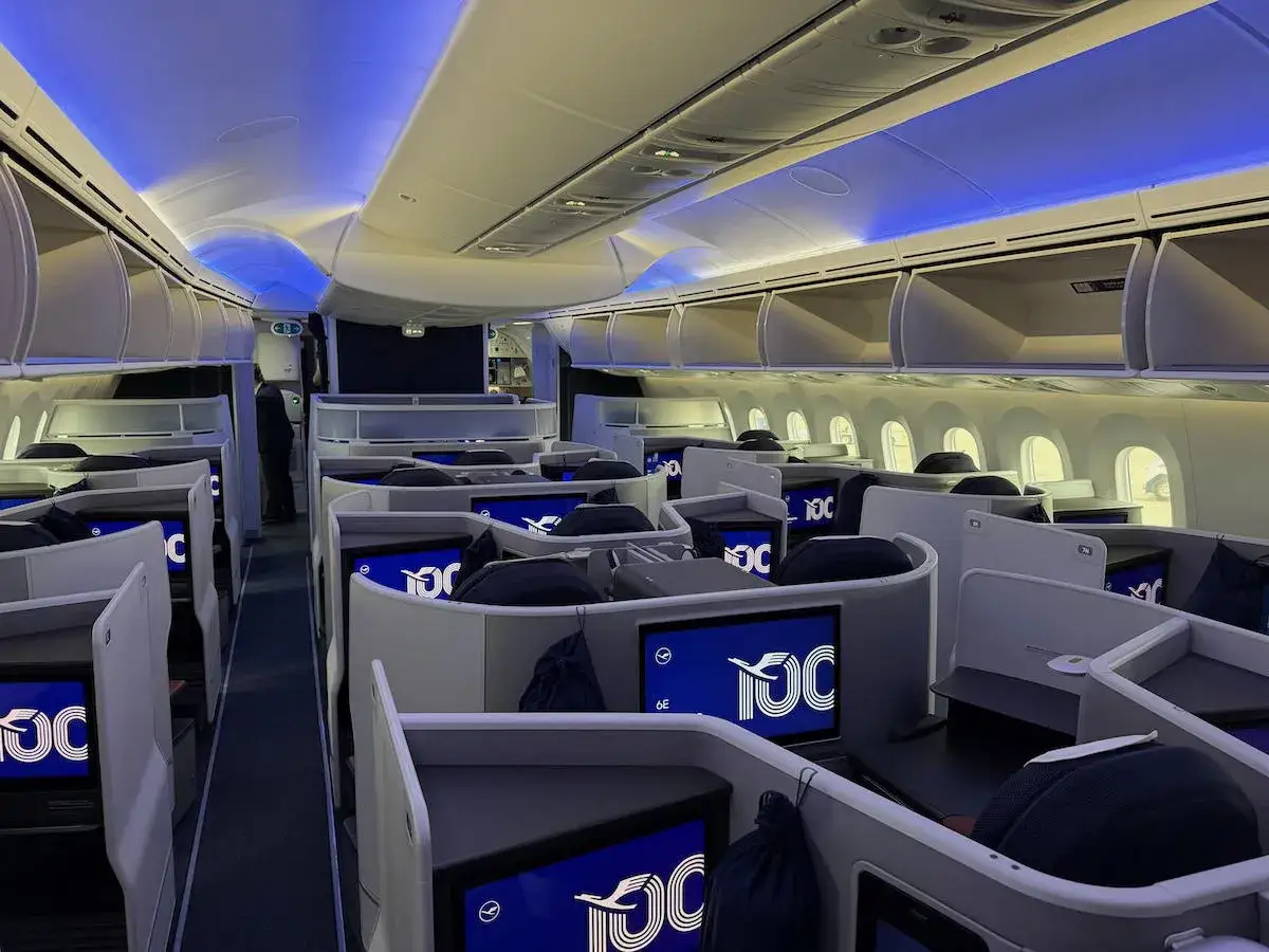 Luxuri&ouml;se Business-Class-Sitze im Dreamliner der Lufthansa. Blaue Akzentbeleuchtung und Bildschirme mit 100-Jahre-Logo.